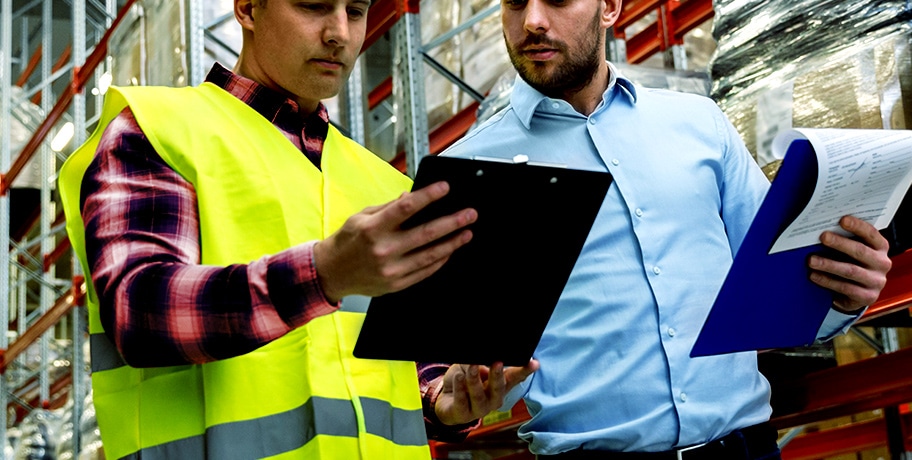 two men in a warehouse looking at clipboards