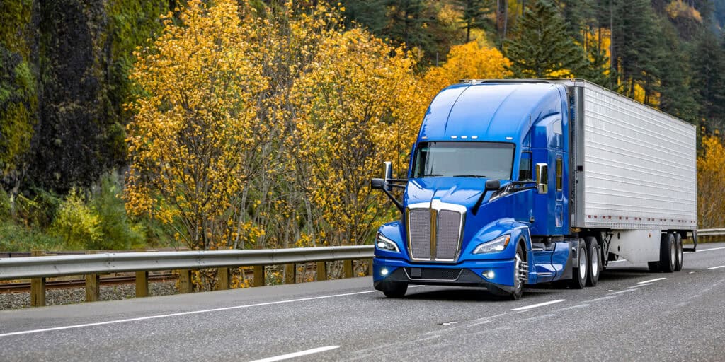 blue freight truck driving in fall foliage on highway